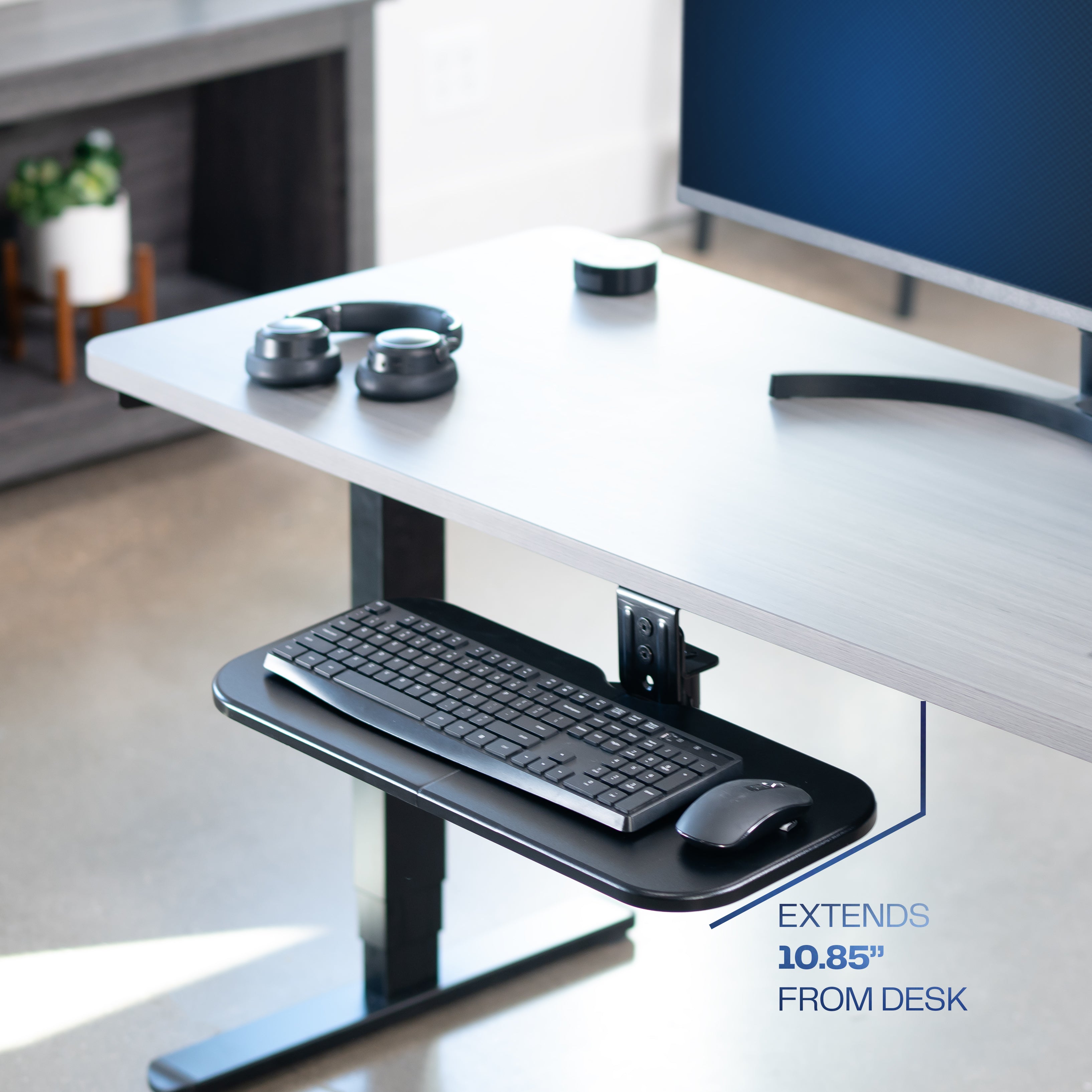 Keyboard tray extending from a desk with a monitor and mouse on a home office background.