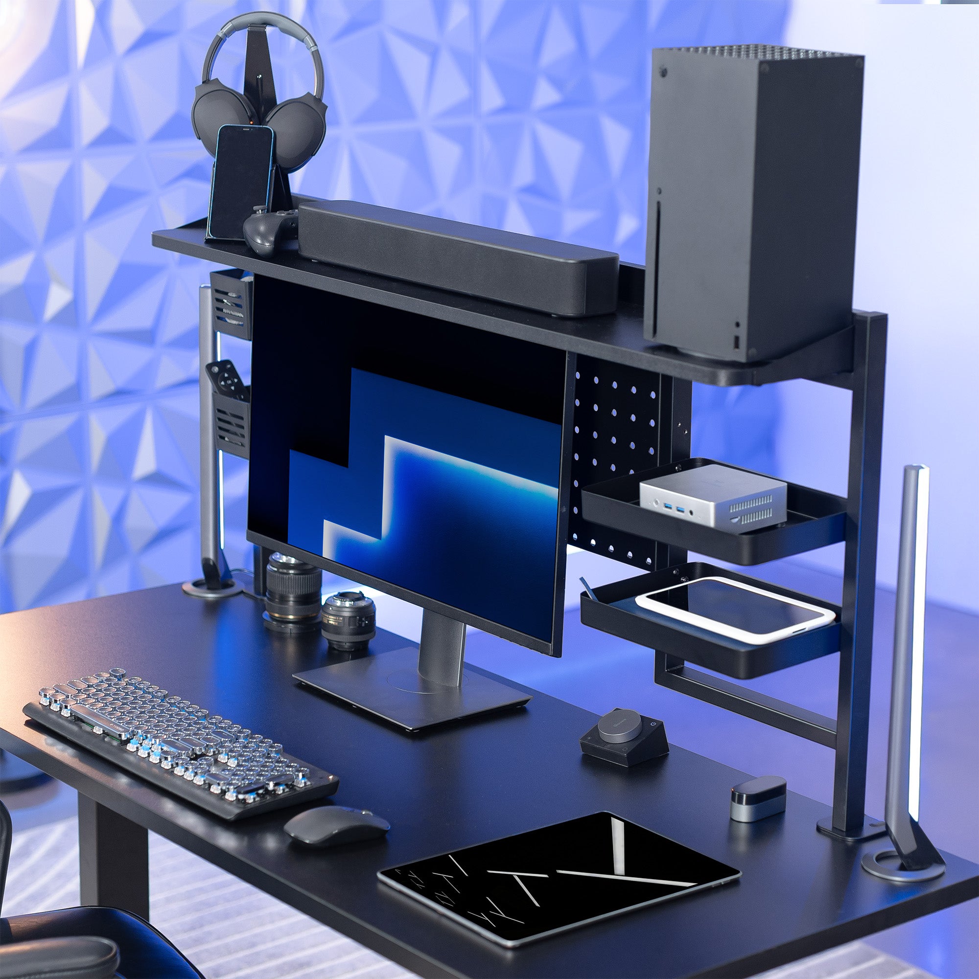 Gaming desk setup with computer monitor, keyboard, mouse, and gaming accessories on a blue geometric background.