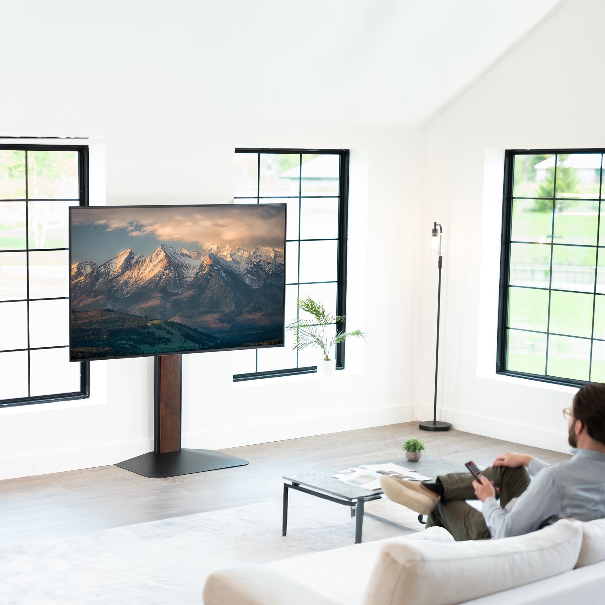 Person sitting on a couch in a modern living room with a large TV displaying mountains.