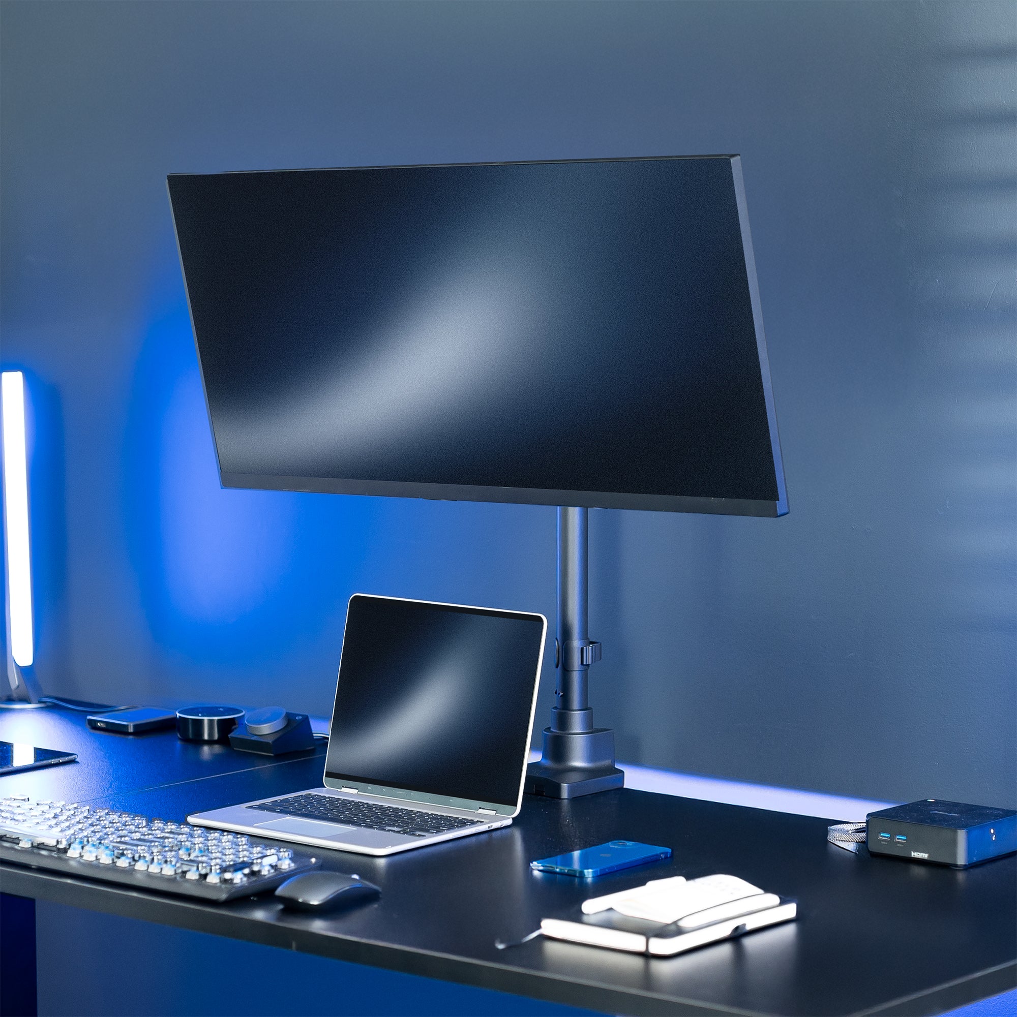Modern office desk setup with a monitor, laptop, and keyboard against a blue wall.