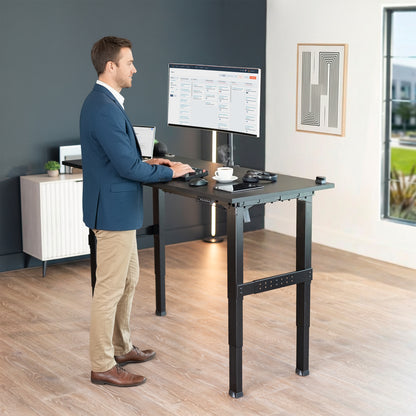 Man standing at Black Premium Electric Dual-Motor Height Adjustable 4-Leg Desk Frame with computer monitor