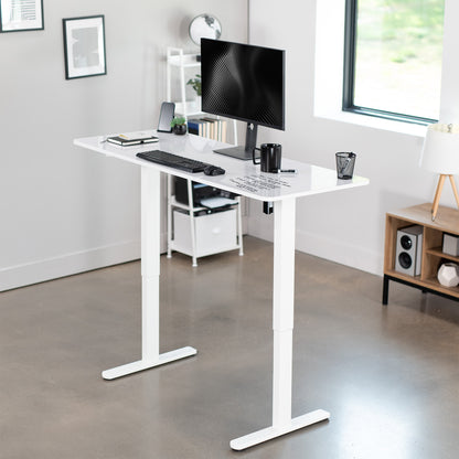 White adjustable desk with computer setup in a modern office.
