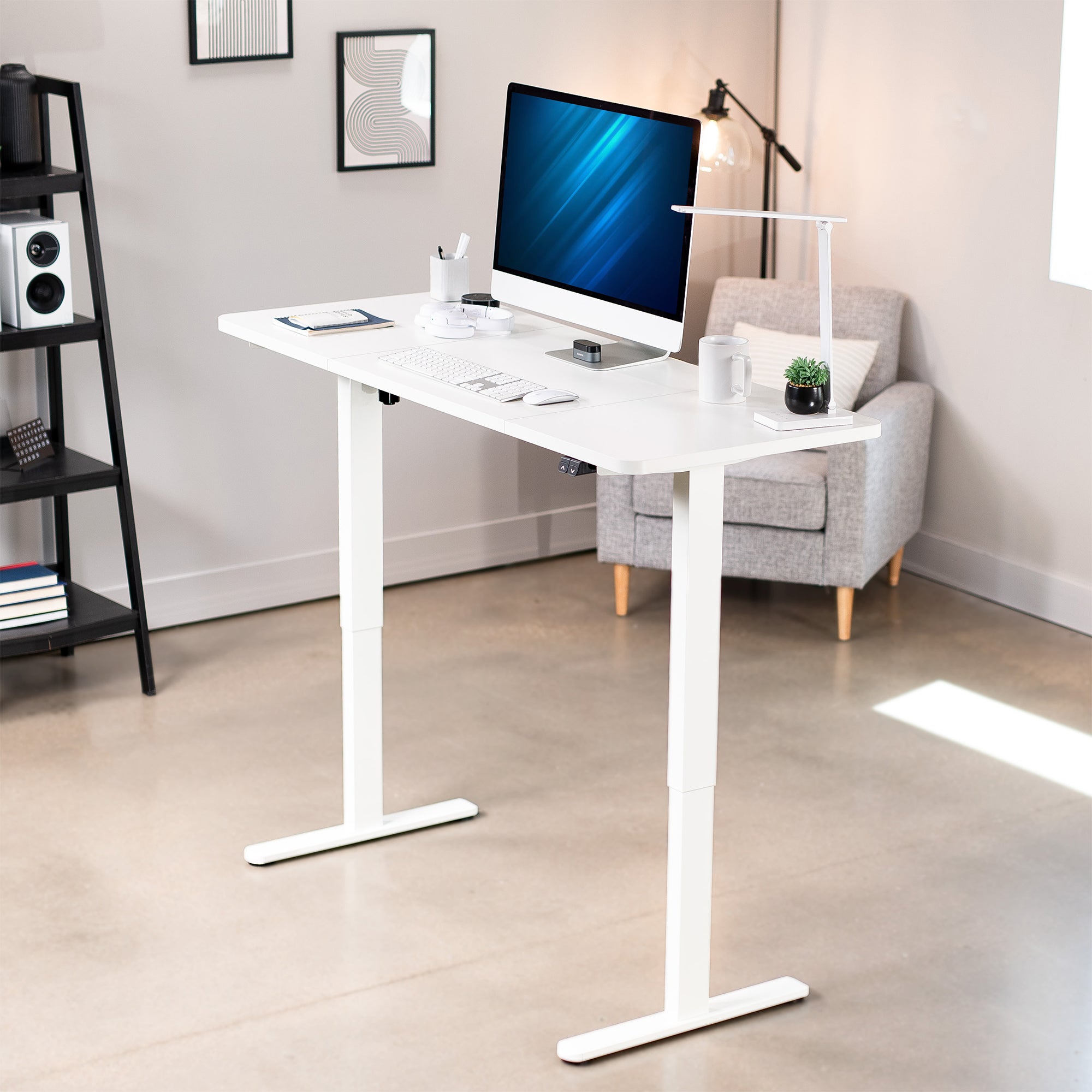 White adjustable desk in a home office setting with a computer monitor, chair, and decor.