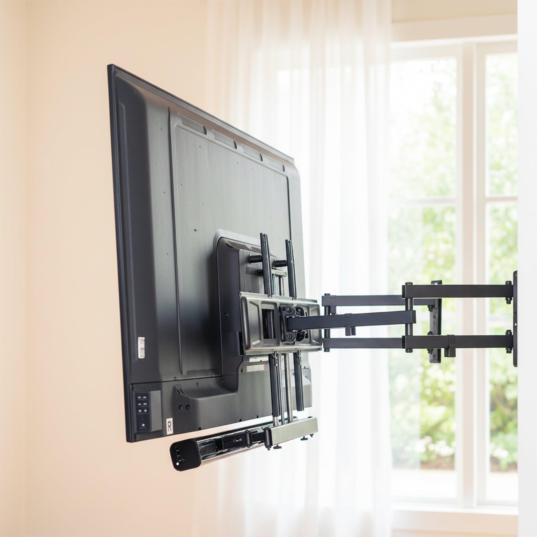 TV mounted on a wall with a bracket in a room with a window featuring a  Soundbar TV Mount