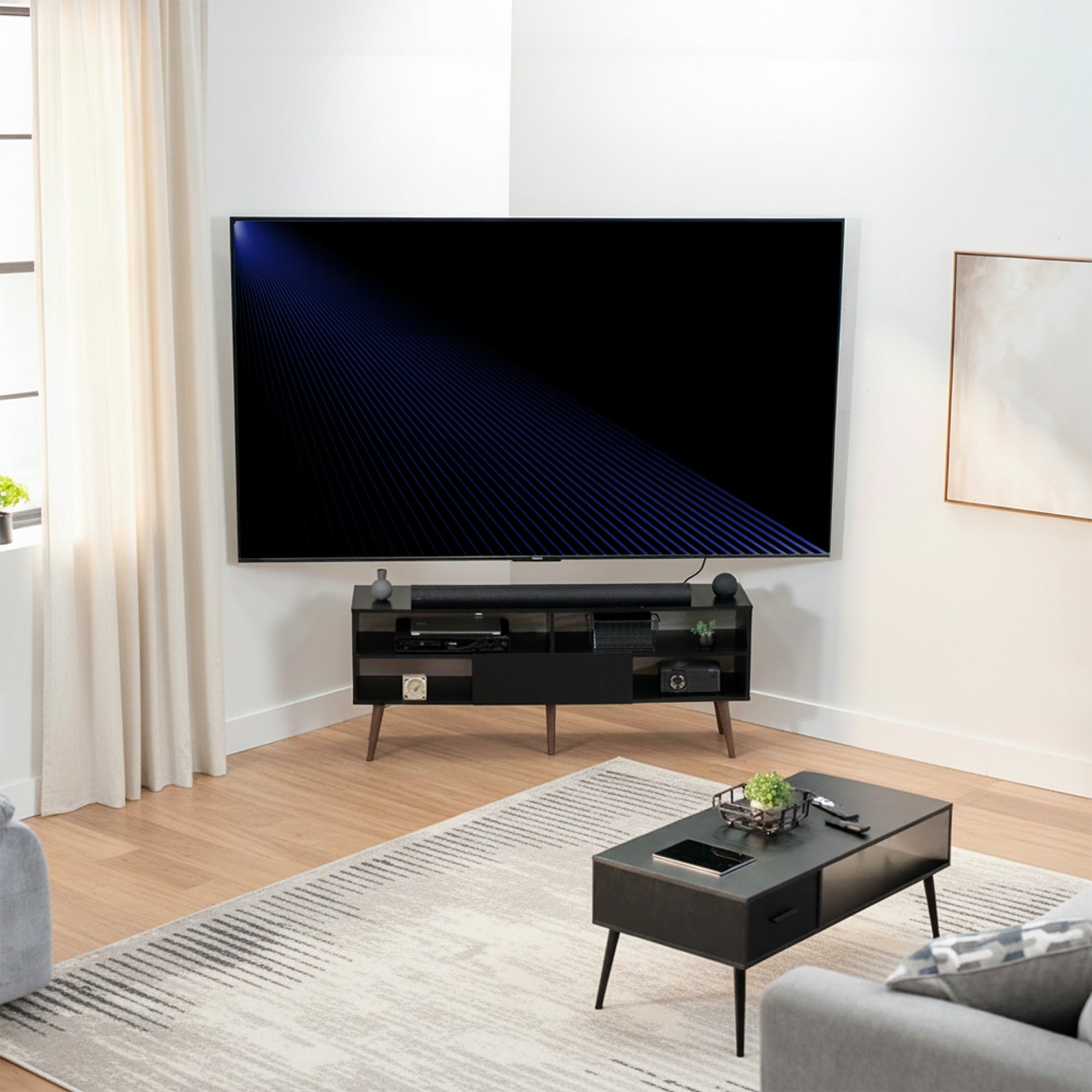 Modern living room with a large TV mounted in corner above a stand, coffee table, and gray sofa.