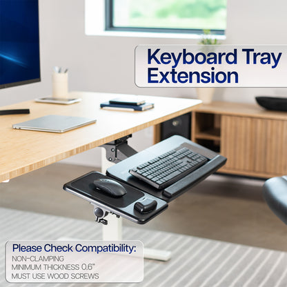 Keyboard tray extension on a desk with a computer setup in the background