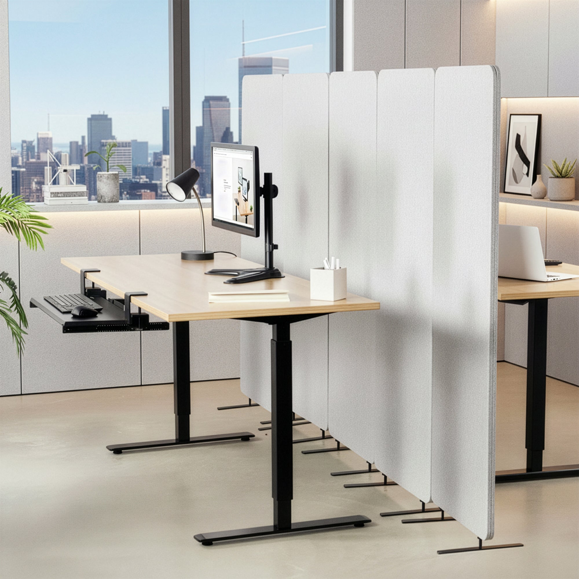 Modern office setup with adjustable desks and a gray partition in between spaces.